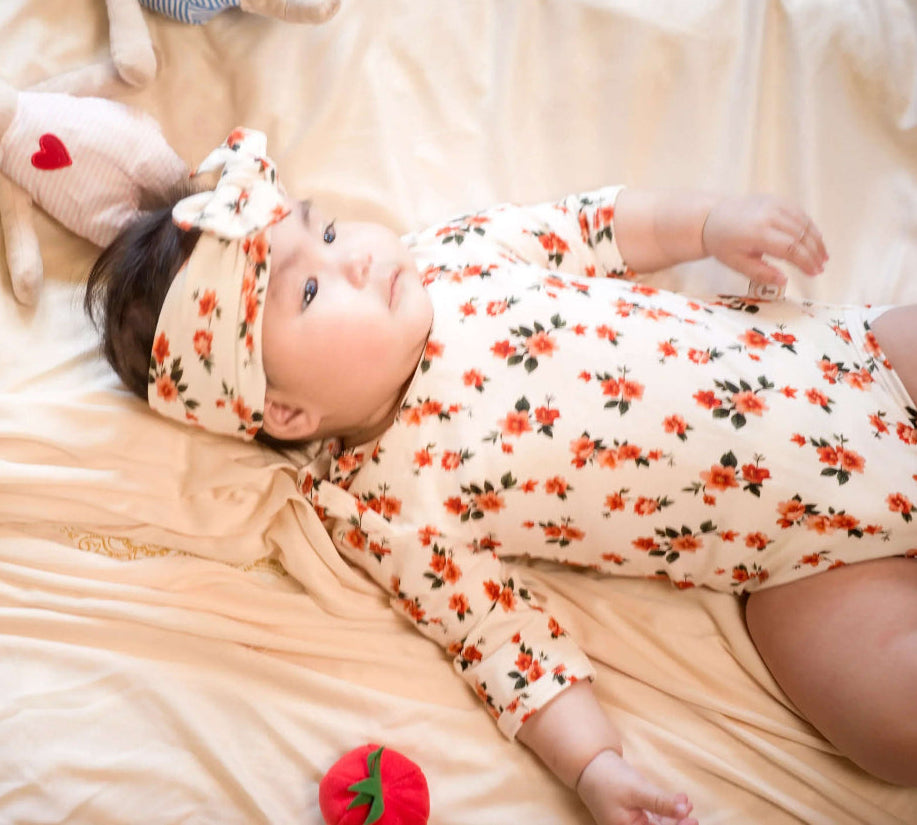 Baby lying on a bed with floral outfit and headband, surrounded by plush toys.
