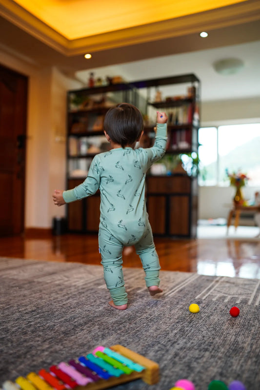 Child wearing the KendiKids Uhuru Sage Zipper Romper — leaping gazelle print on sage green