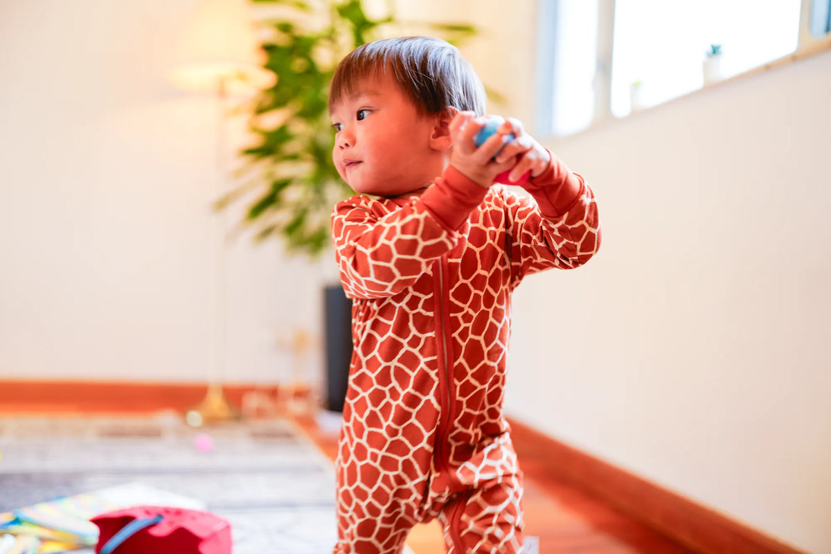 Toddler standing indoors in the KendiKids Twiga Zipper Romper — giraffe print in burnt orange