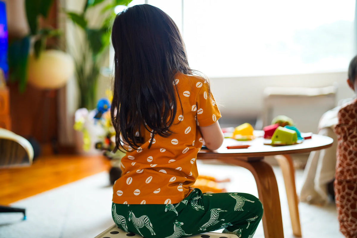 Child wearing the KendiKids Baraka Short-Sleeved Tee — cowrie shell print on mustard