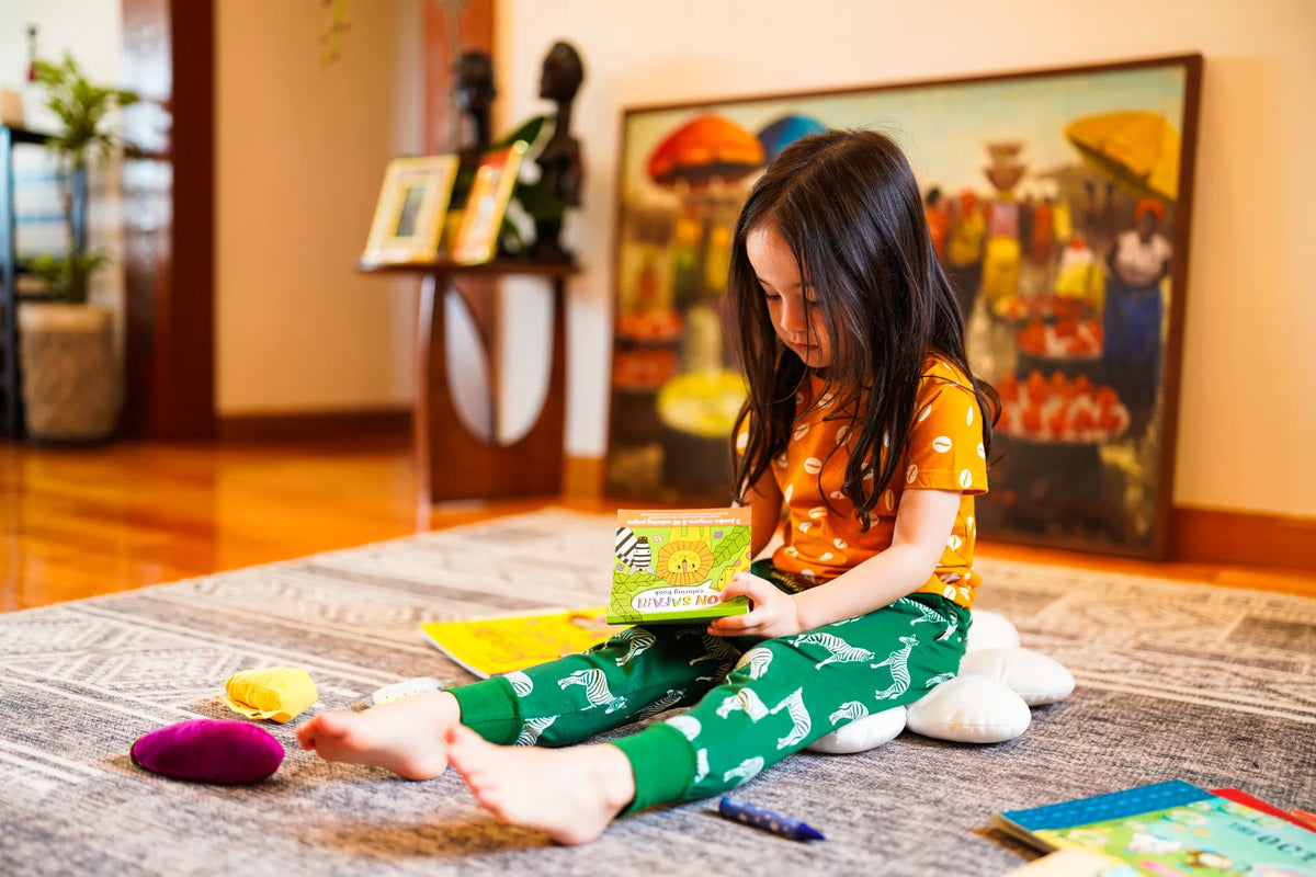 Toddler girl sitting on a rug playing in KendiKids Ndoto Joggers — zebra print in white on forest green
