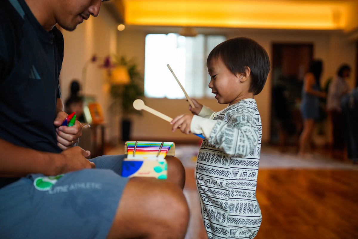 Toddler and parent playing a toy xylophone, toddler in the KendiKids Asili Zipper Romper — mud cloth print in black on cream