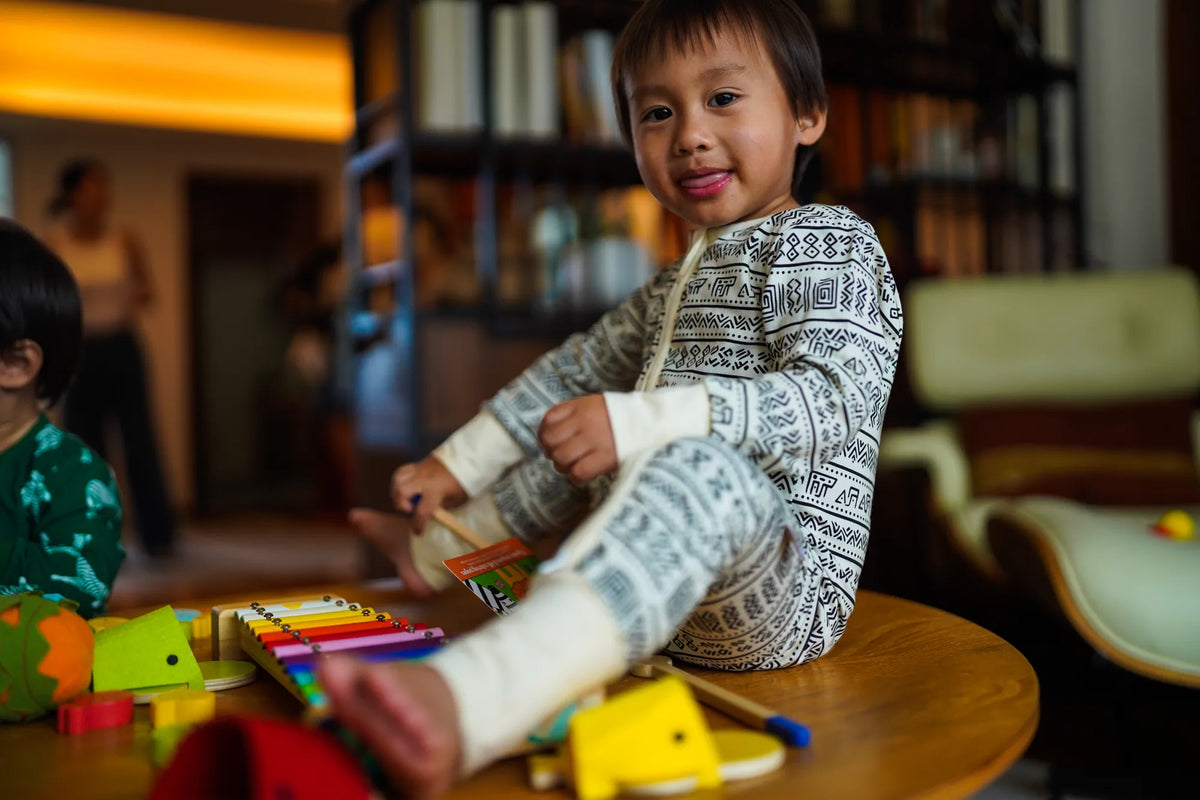Toddler playing with toys at a low table in the KendiKids Asili Zipper Romper — mud cloth print in black on cream
