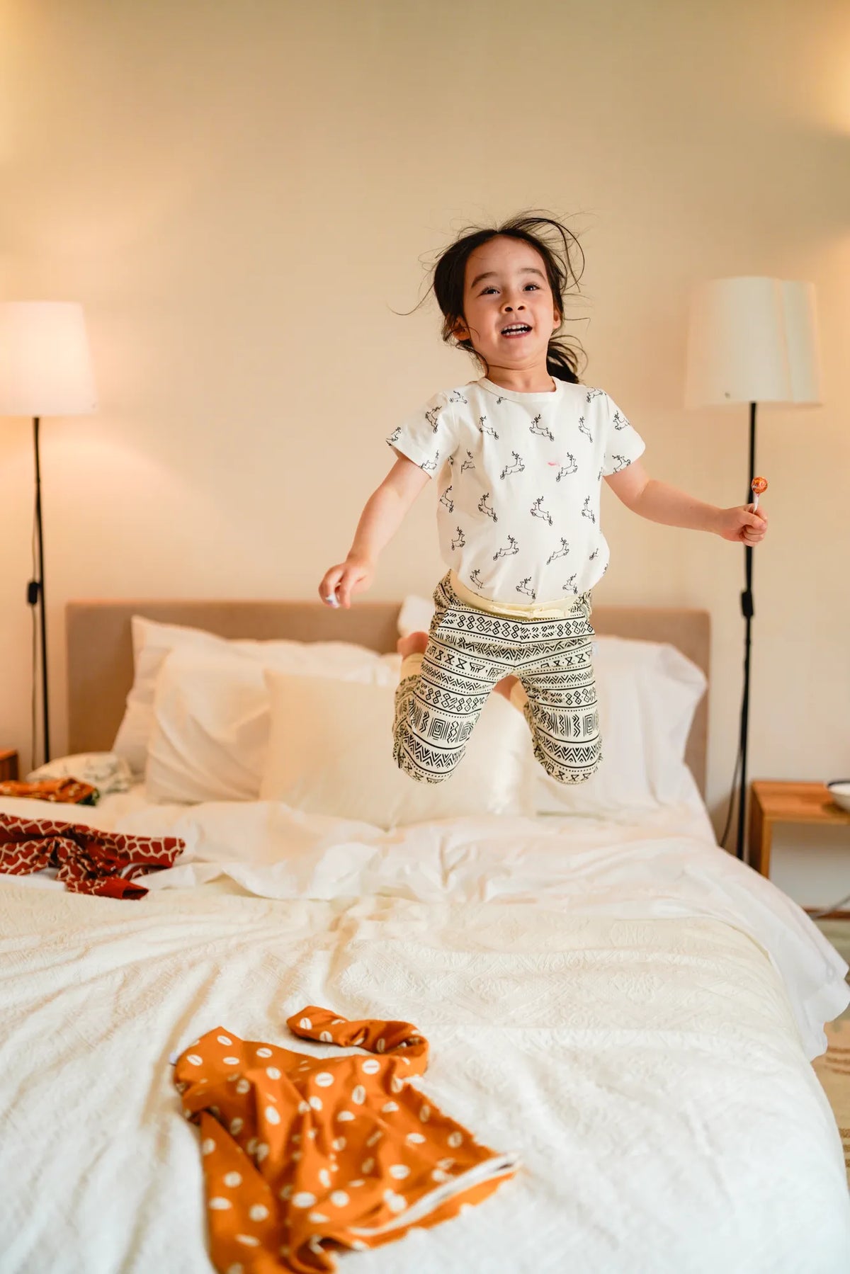 Toddler girl jumping on a white bed in KendiKids Asili Joggers — mud cloth print in black on cream