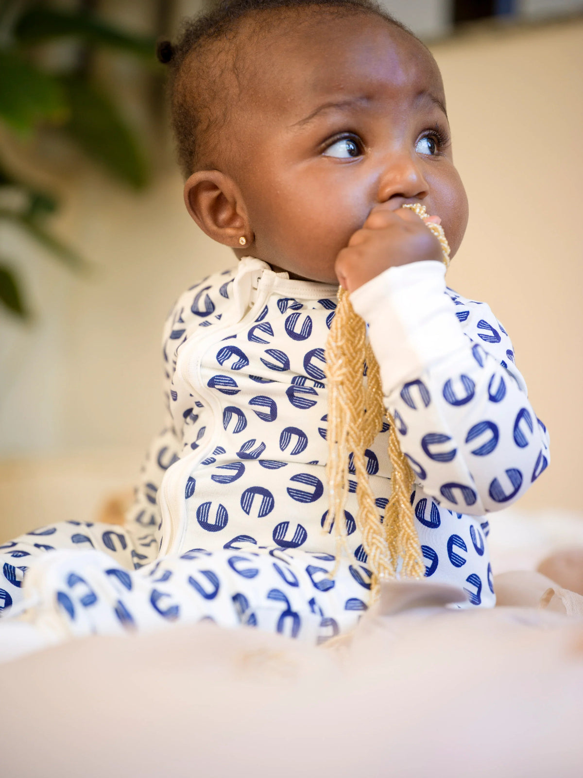 Baby wearing a blue and white patterned romper with a textured garment, sitting on a beige surface.