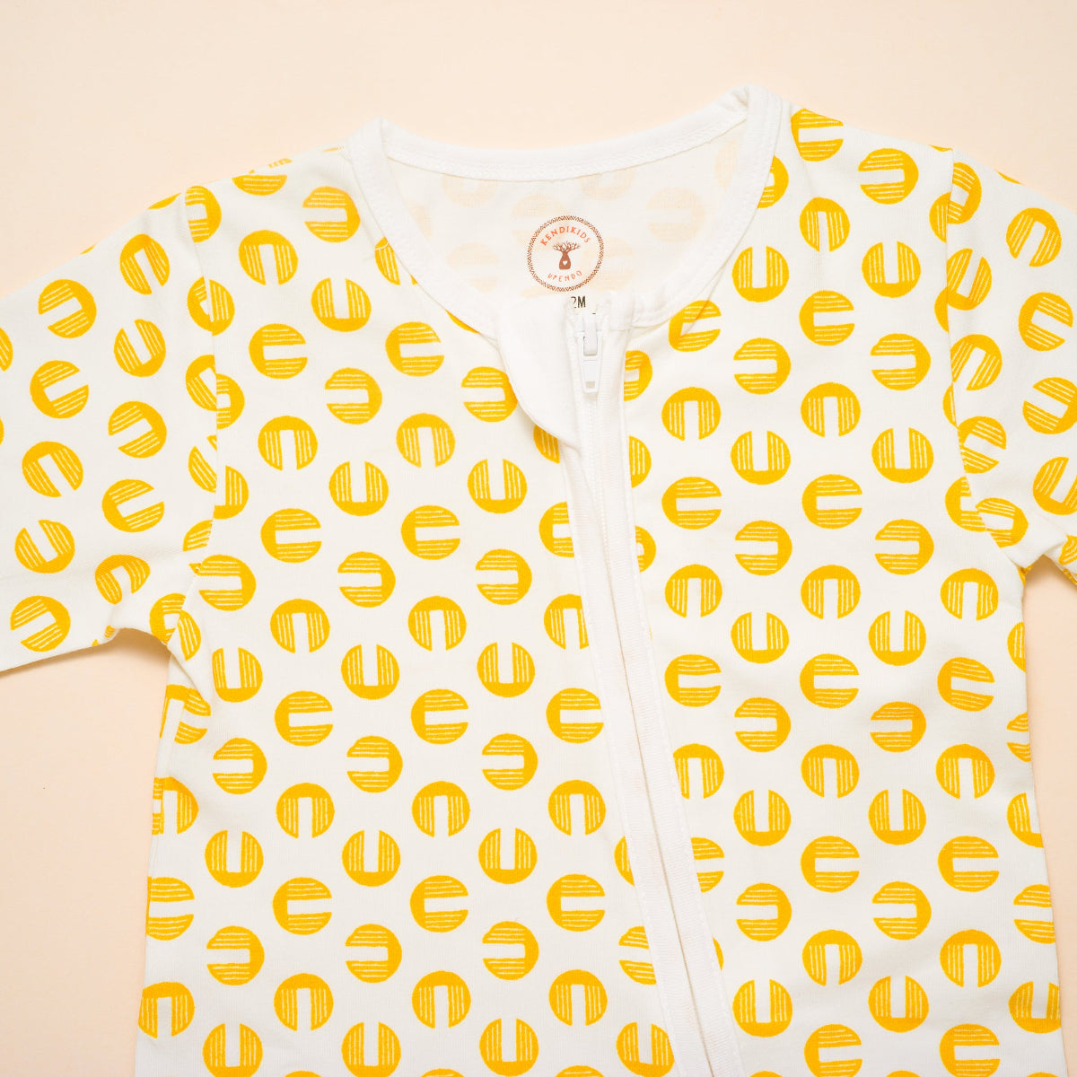 White baby onesie with yellow pattern on a beige background