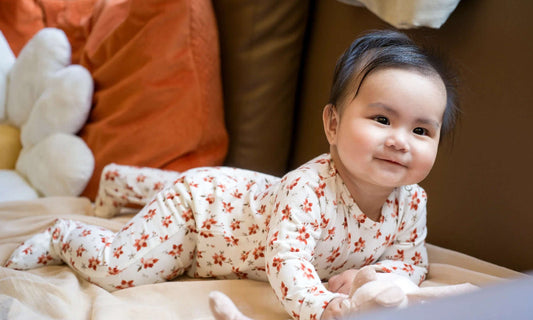 Baby in a floral onesie, romper  lying on a couch with colorful pillows