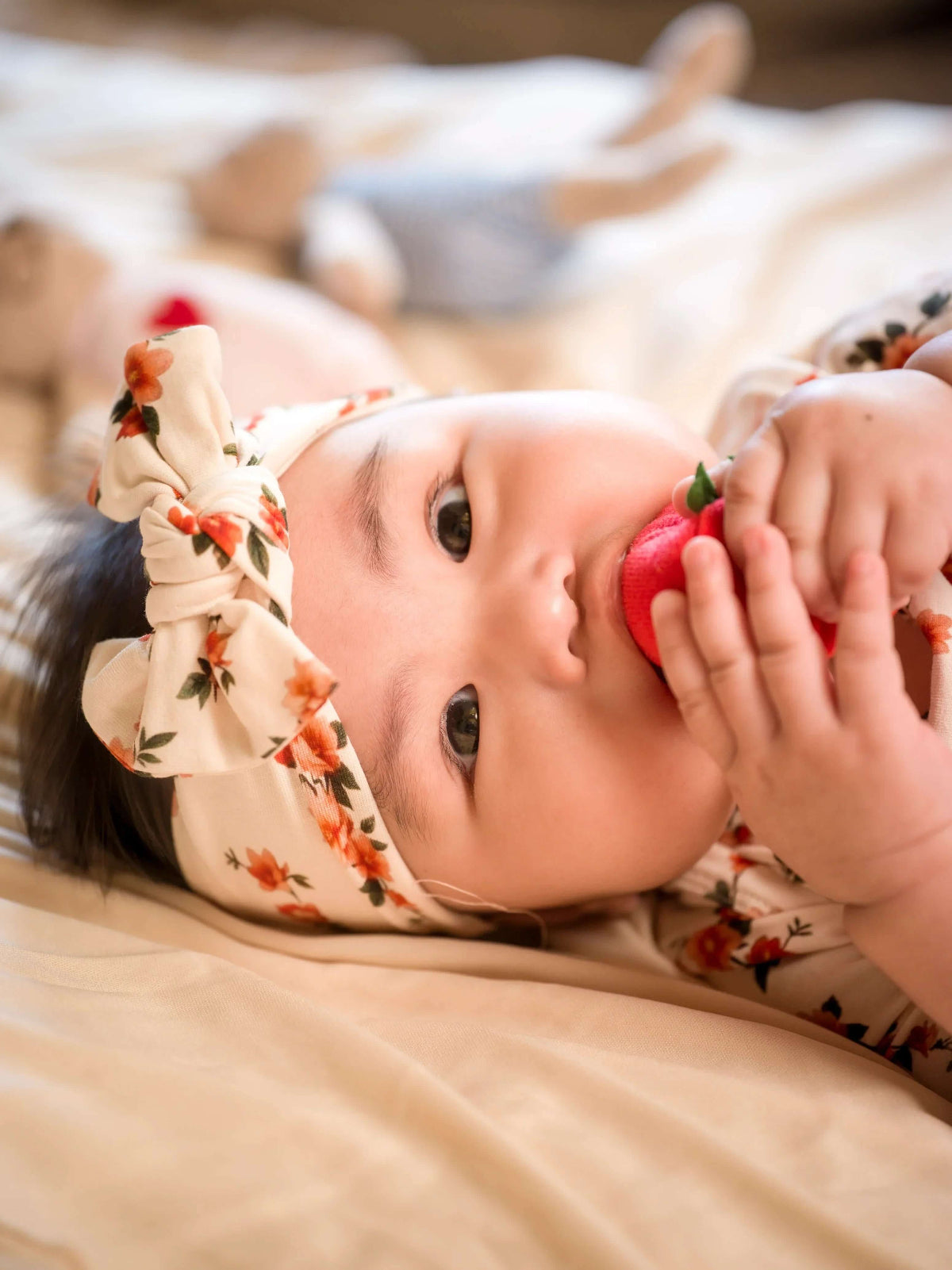 Baby lying on a bed holding a red toy