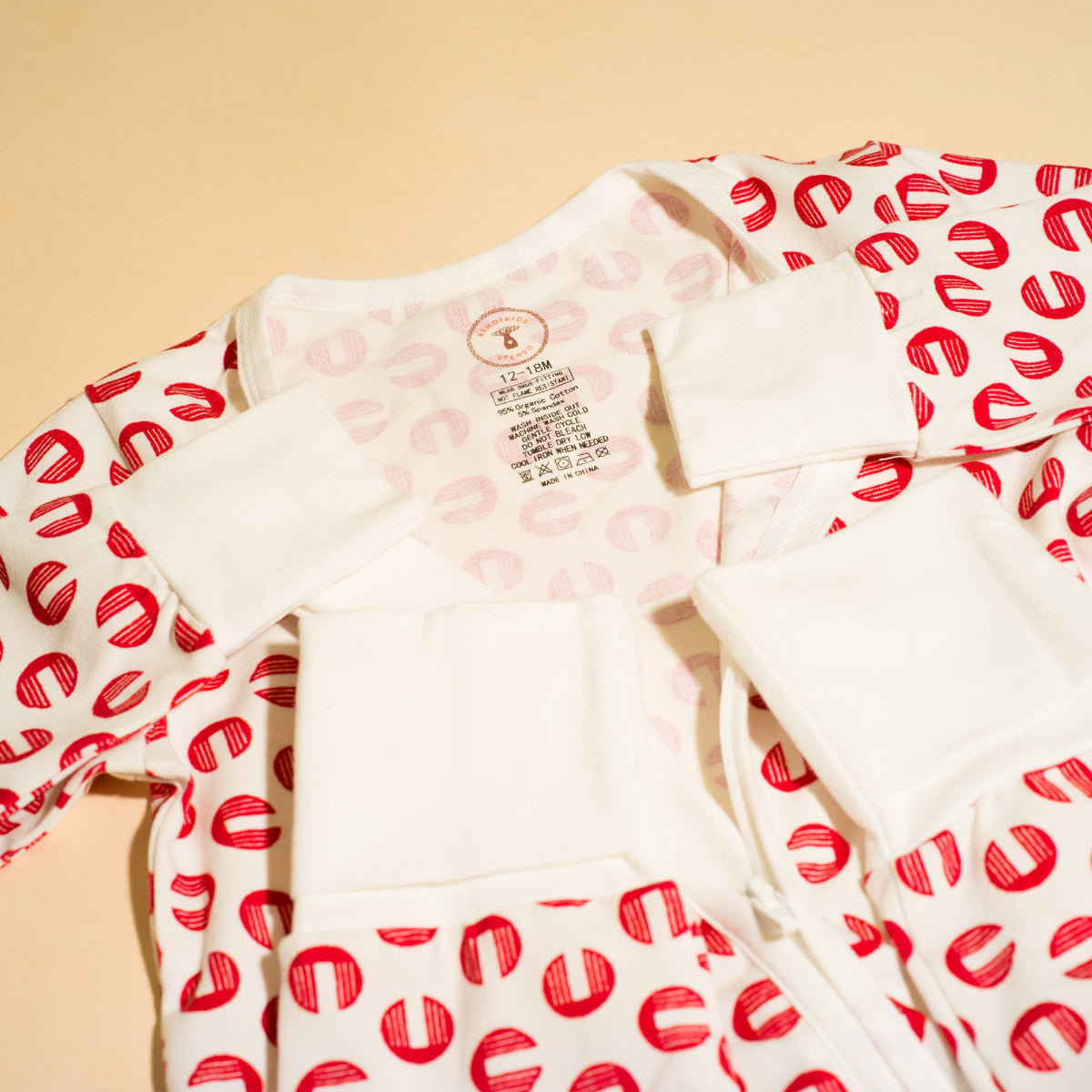 White romper with red pattern on sleeves against a beige background