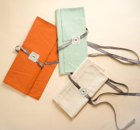 Three fabric bags in orange, green, and beige with straps on a beige background