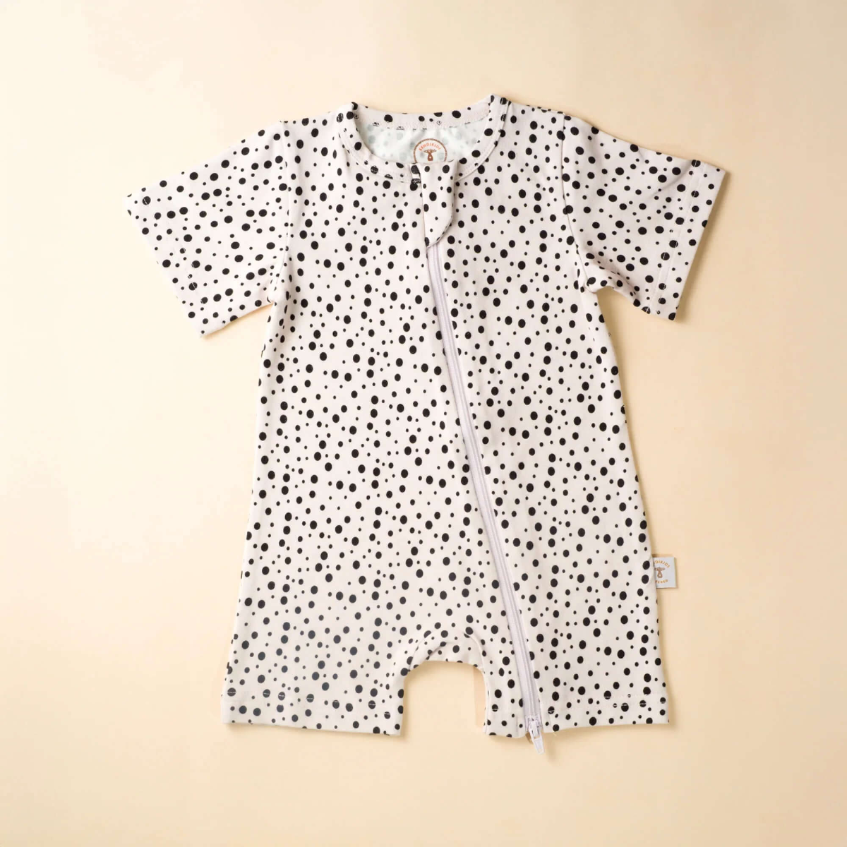 Baby romper with black polka dot pattern on a beige background