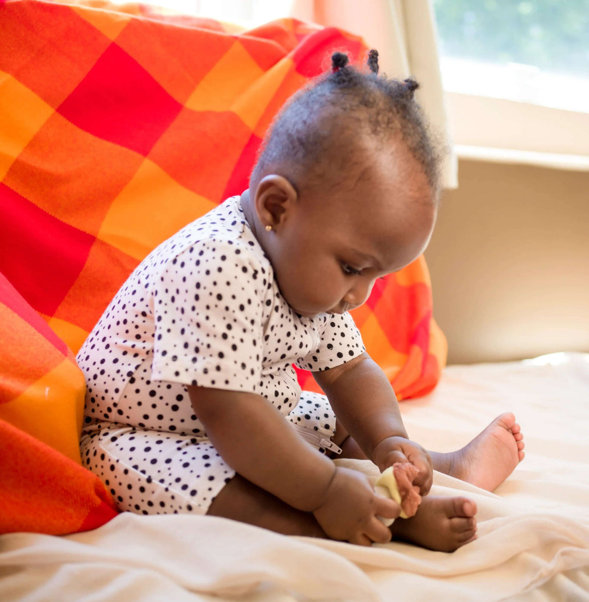 Baby sitting on a bed with a colorful blanket in the background wearing kendikids organic cotton short romper