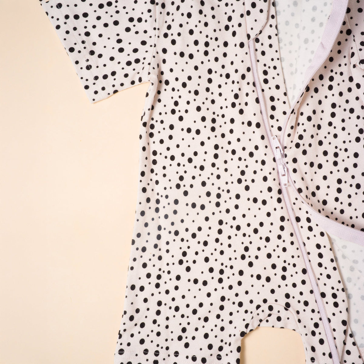 Polka dot baby romper with a zipper on a beige background