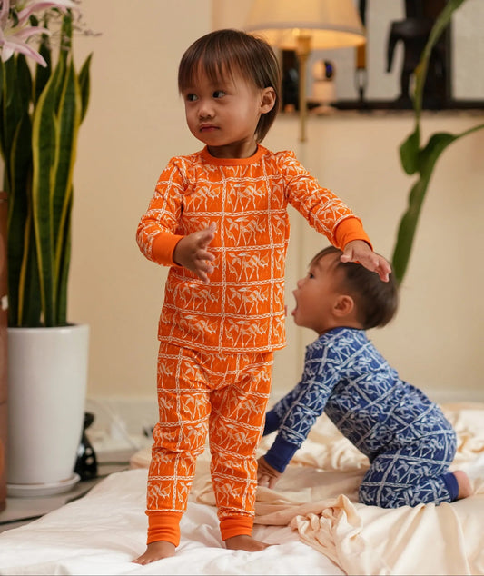 Three children in pajamas on a bed with plants and decor in the background