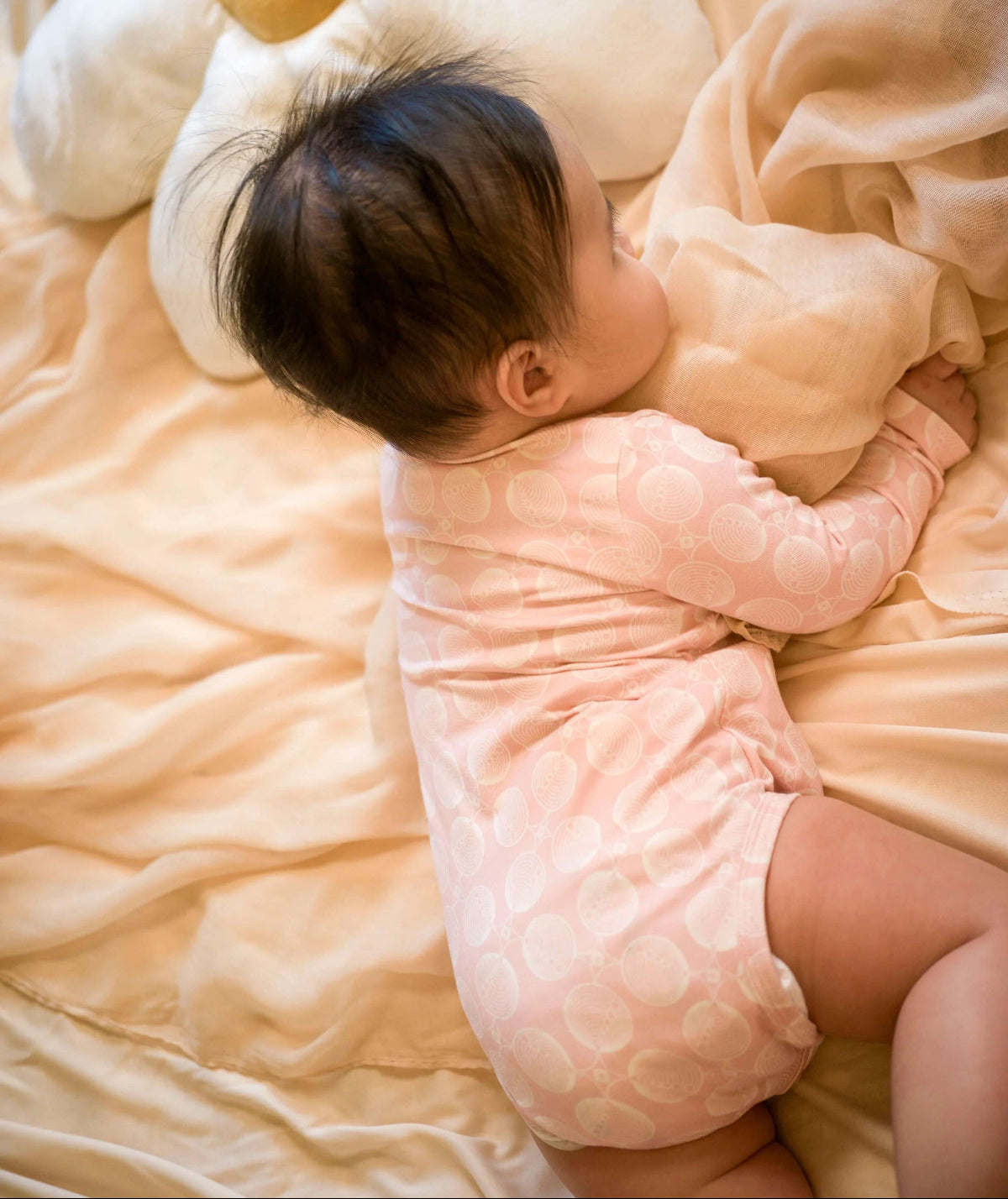 Newborn baby wrapped in a pink bodysuit on a soft surface