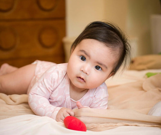 Baby lying on a bed with a red toy, wearing a pink bodysuit