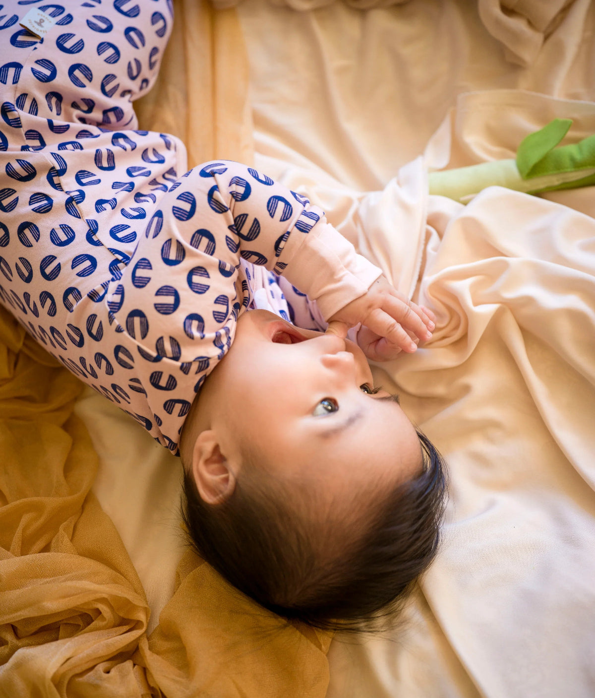 Baby lying on a beige blanket wearing a patterned romper  outfit
